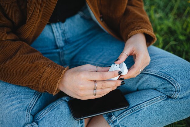 Uma mulher abrindo a caixa de carregamento de fones de ouvido sem fio enquanto está sentada na grama