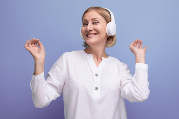 Uma mulher adulta com um penteado loiro dança ao som da música em fones de ouvido sem fio