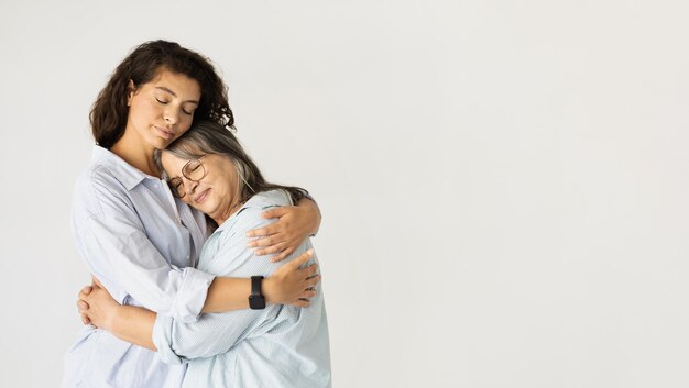 Foto uma mulher adulta positiva abraçando uma senhora idosa desfruta de um estilo de vida amoroso isolado no fundo branco do estúdio