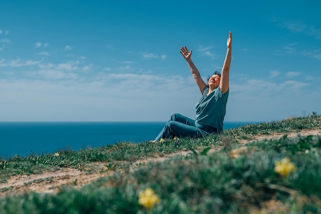 Foto uma mulher adulta senta-se em uma montanha descalça levantando as mãos para o céu e o sol em um dia ensolarado