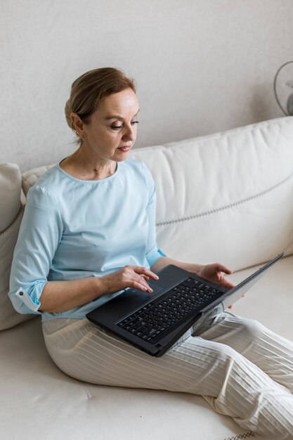 Foto uma mulher adulta sentada no sofá em seu colo ela tem um laptop preto vertical