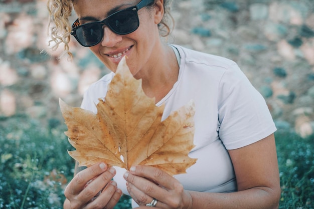 Uma mulher adulta serena e feliz sorri e admira a grande folha de bordo de outono no jardim em atividade de lazer ao ar livre Conceito de botânica e jardinagem Mulheres alegres desfrutam do sorriso natural ao ar livre