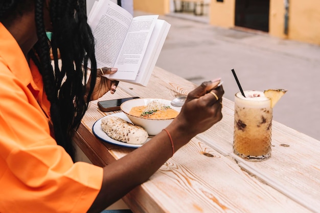 Uma mulher afro-americana irreconhecível lendo um livro enquanto almoçava vegetariano
