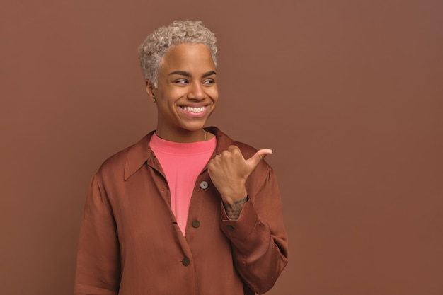 Uma mulher afro-americana positiva em um sorriso casual vestido aponta para o lado