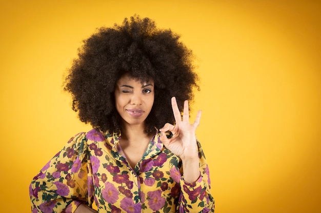 Uma mulher afro-americana sorridente e alegre olha por meio de um gesto de zero ou ok