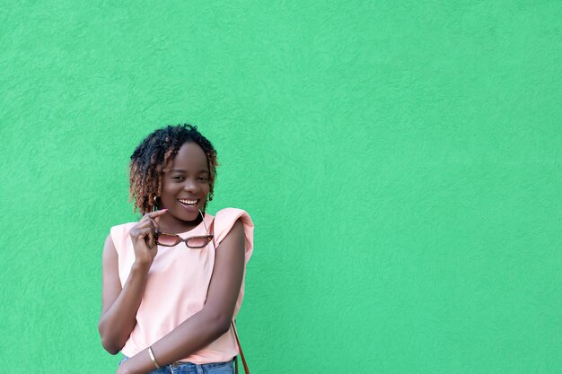 Uma mulher afro-americana sorridente feliz com óculos nas mãos em um fundo verde copiar espaço