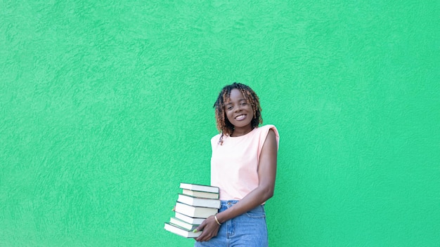 Uma mulher afro-americana sorridente segura uma pilha de livros em um fundo verde Copiar espaço Educação