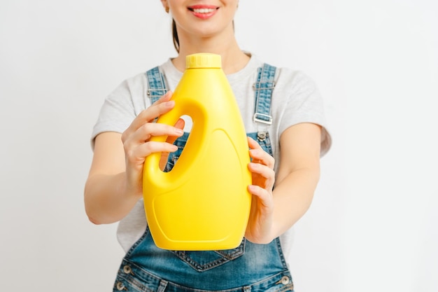 Foto uma mulher alegre em trajes casuais exibindo uma garrafa de detergente em branco amarelo vibrante mockup para design