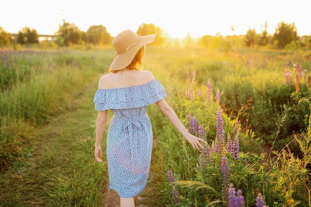 Uma mulher anda pelo campo toca os tremoços com a mão e olha para o pôr do sol