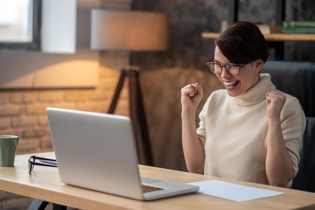 Uma mulher animada sentada no laptop e esperando as atualizações