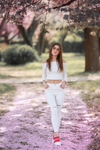 Uma mulher ao ar livre em um jardim com uma flor de cerejeira rosa caminha por todo o caminho ao longo de um caminho repleto de flores cor de rosa