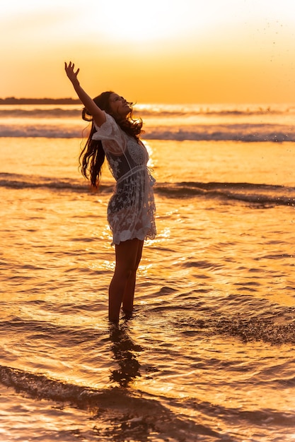 Uma mulher ao pôr do sol em um vestido branco, aproveitando a água do mar no verão