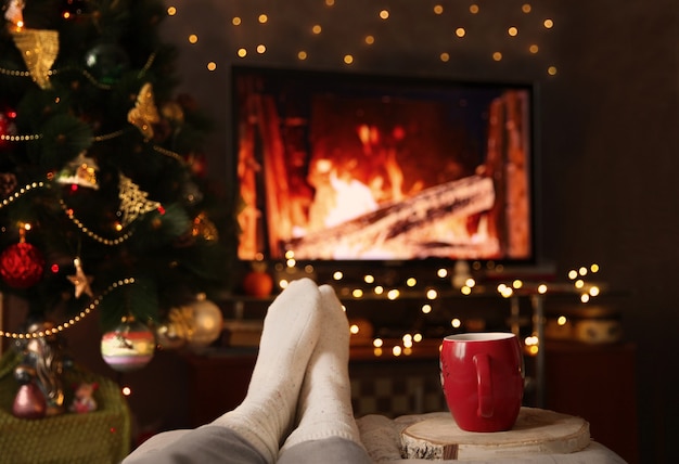 Uma mulher aquece os pés em meias junto à lareira com uma xícara de bebida quente Conceito de férias de inverno