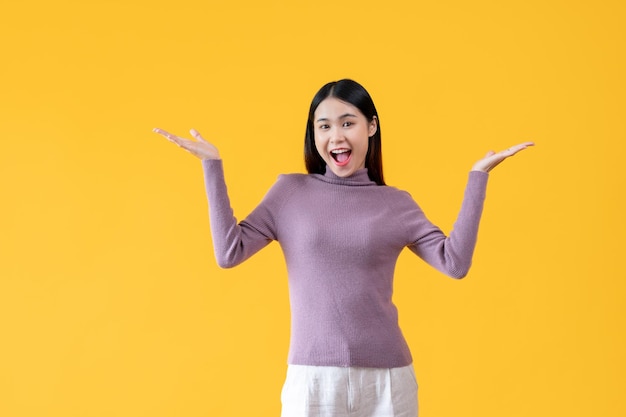 Uma mulher asiática alegre e animada está abrindo as palmas das mãos em um estúdio amarelo isolado