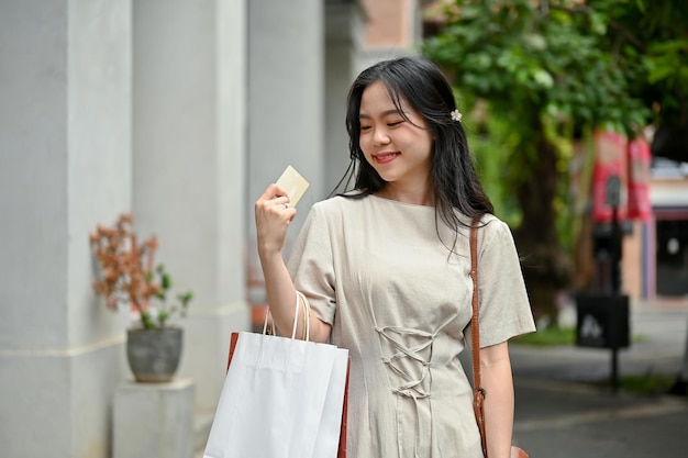 Uma mulher asiática atraente está aproveitando seu dia de compras na cidade segurando seu cartão de crédito