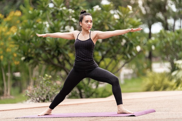 Uma mulher asiática de meia-idade confiante com roupa de esporte, fazendo exercícios de ioga no tapete de ioga ao ar livre no quintal de manhã. Mulher jovem fazendo exercícios de ioga ao ar livre no parque público natural