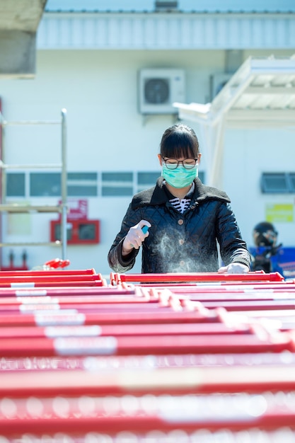 Uma mulher asiática de óculos pulverizando álcool na alça de um carrinho de compras para limpar e matar o vírus b