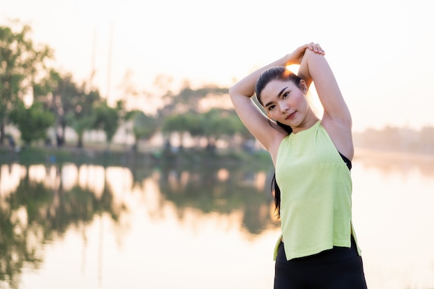 Uma mulher asiática em roupas esportivas fazendo alongamento antes do treino ao ar livre no parque