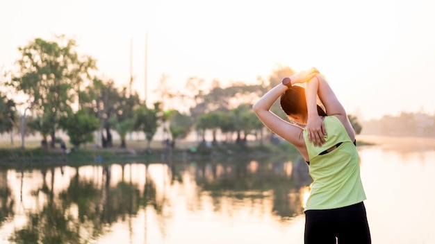 Uma mulher asiática em roupas esportivas fazendo alongamento antes do treino ao ar livre no parque