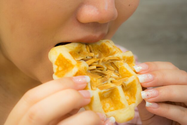 Uma mulher asiática está comendo waffle de amêndoa.