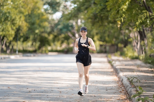 Uma mulher asiática feliz e saudável, em trajes esportivos pretos, correndo no parque natural da cidade sob o pôr do sol