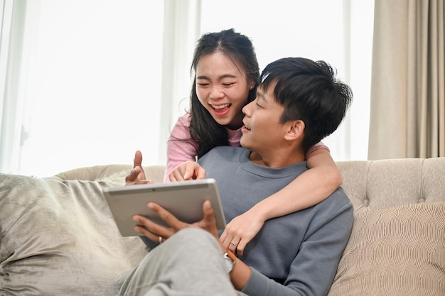 Uma mulher asiática feliz está abraçando seu noivo por trás enquanto assistem a algo juntos em um tablet