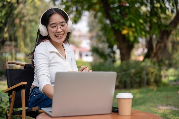 Uma mulher asiática feliz está trabalhando em suas tarefas em seu laptop enquanto está sentada em seu quintal