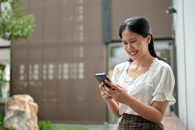 Uma mulher asiática feliz usando seu smartphone conversando com seus amigos enquanto relaxa no parque
