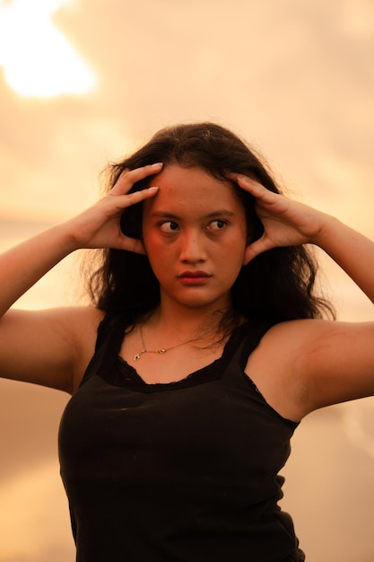 Uma mulher asiática posa com uma expressão ousada e sexy enquanto veste roupas pretas em frente à praia