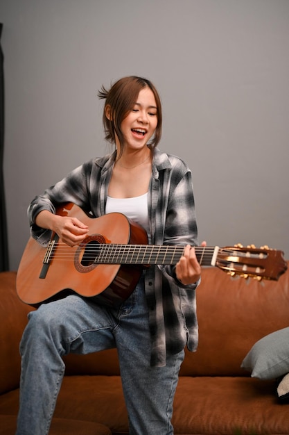 Uma mulher asiática talentosa canta enquanto toca seu violão na sala de estar