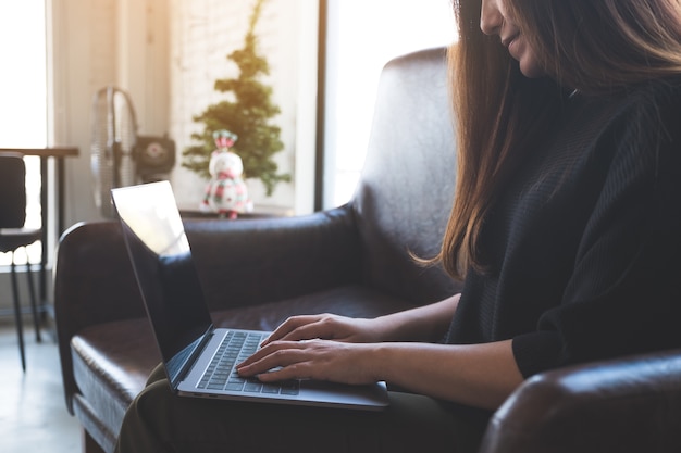 Uma mulher asiática trabalhando e digitando no teclado do laptop enquanto está sentado no sofá