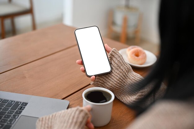 Uma mulher asiática usando seu smartphone para ler notícias online ou conteúdo tomando café