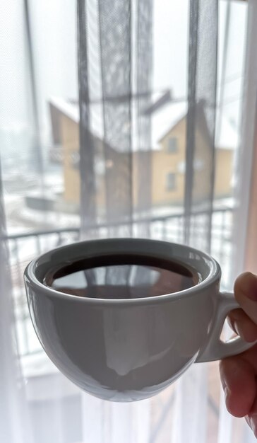 Uma mulher bebe café em uma casa com janelas A garota gosta da calma recreação da natureza de inverno