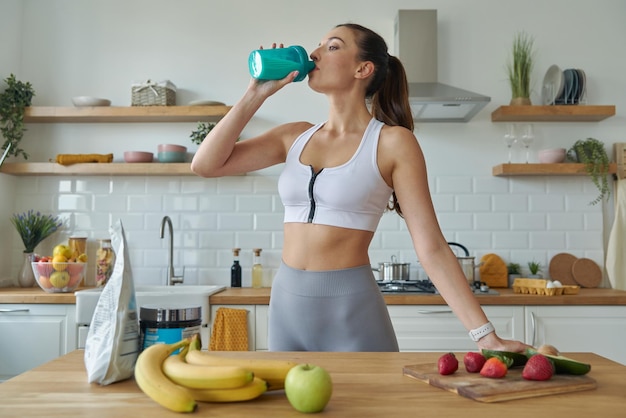 uma mulher bebendo de uma garrafa verde de água com bananas na mesa
