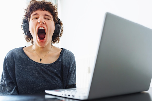 Uma mulher boceja na frente de um laptop com um laptop aberto.