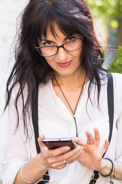 Uma mulher bonita e elegante em óculos usa um smartphone.