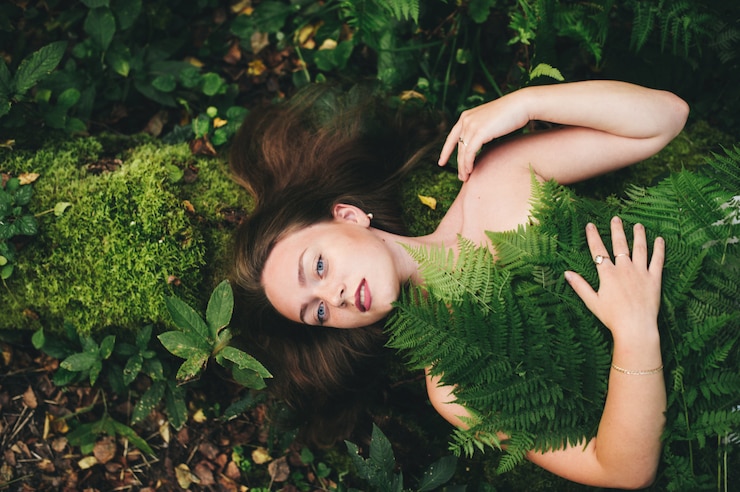 Foto uma mulher bonita em um vestido floral está sentada com um buquê de samambaia na floresta.