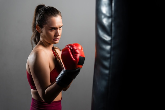 Uma mulher boxer em um agasalho vermelho atinge um saco de pancadas em um fundo escuro