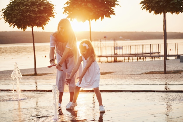 Uma mulher brincando com uma criança perto do mar no parque ao pôr do sol