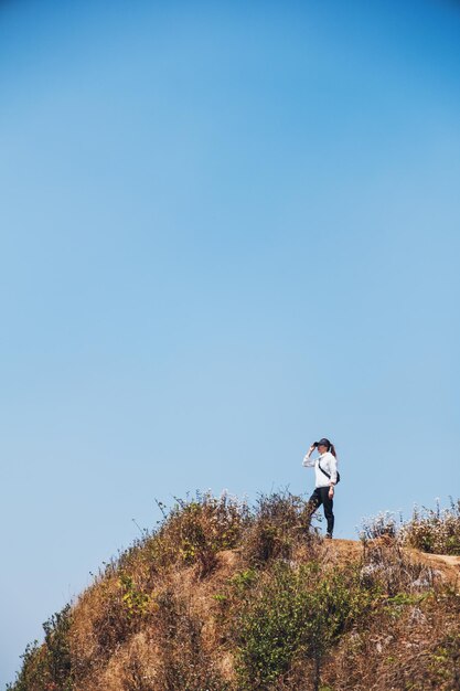 Uma mulher caminhando e de pé no topo de uma montanha com um fundo de céu azul