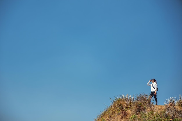 Uma mulher caminhando e de pé no topo de uma montanha com um fundo de céu azul