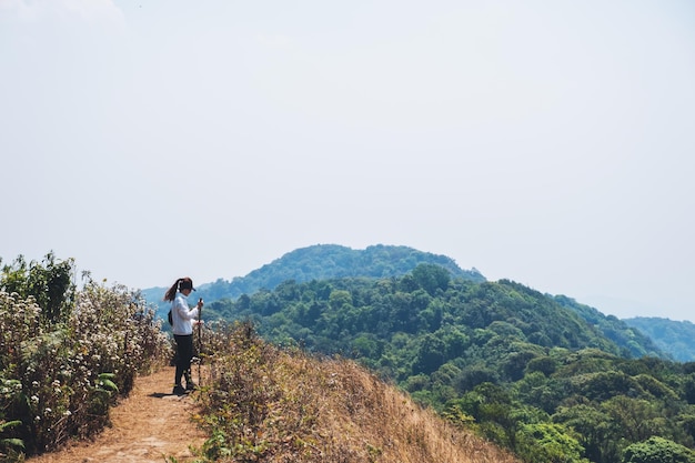 Uma mulher caminhando e de pé no topo de uma montanha com um fundo de céu azul