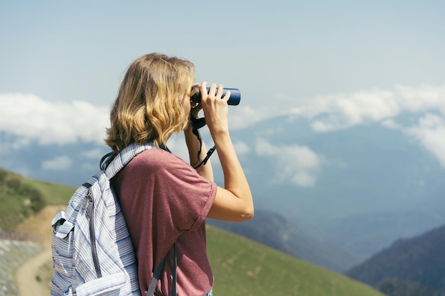 Foto uma mulher caminhando olha através de binóculos enquanto está de pé no alto das montanhas