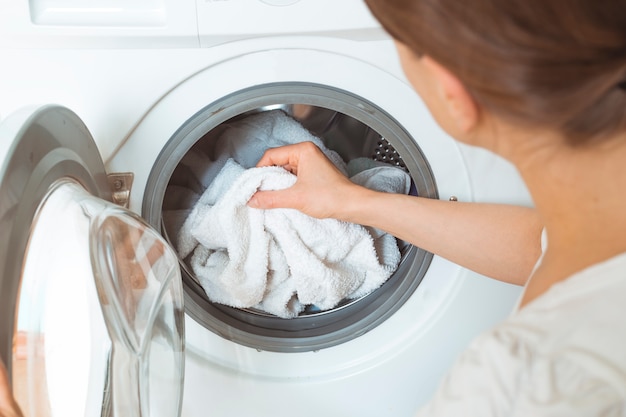 Uma mulher carrega roupas sujas para uma máquina de lavar roupa.