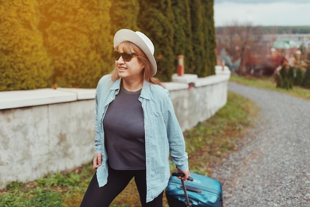 Uma mulher caucasiana adulta com óculos escuros de chapéu e uma camiseta azul chegou ao local de assentamento em habitação alugada Conceito de viagem