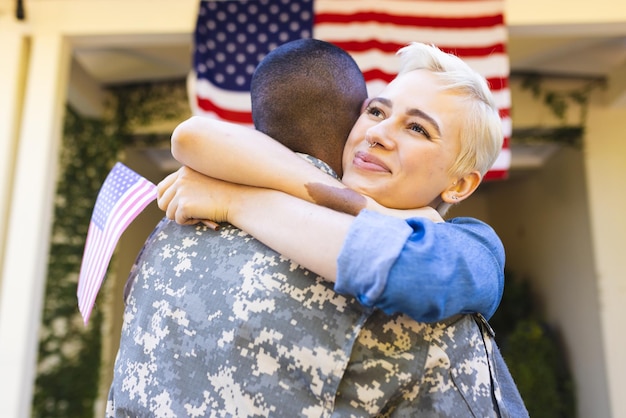 Foto uma mulher caucasiana feliz e um soldado americano mestiço abraçando-se fora da casa. bandeira americana, regresso a casa, patriotismo e serviço militar.