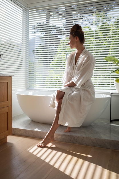 Uma mulher caucasiana passando um tempo em casa, vestindo um roupão de banho, sentada na banheira. Estilo de vida em casa isolando, distanciamento social em quarentena durante a pandemia de coronavírus covid 19.