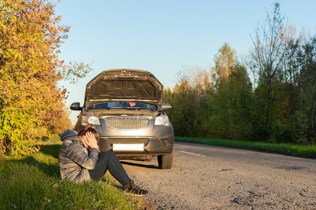 Foto uma mulher chateada está perto de seu carro quebrado e falando ao celular na estrada no outono.