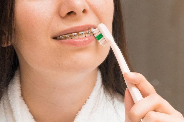 Uma mulher com aparelho ou suporte escovando os dentes com uma escova rosa no banheiro