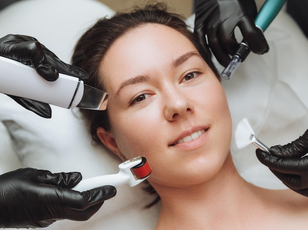Uma mulher com as mãos de vários terapeutas com dispositivos de cosmetologia perto de seu rosto uma mulher precisa de cuidados com a pele foto do conceito de cuidados com a pele